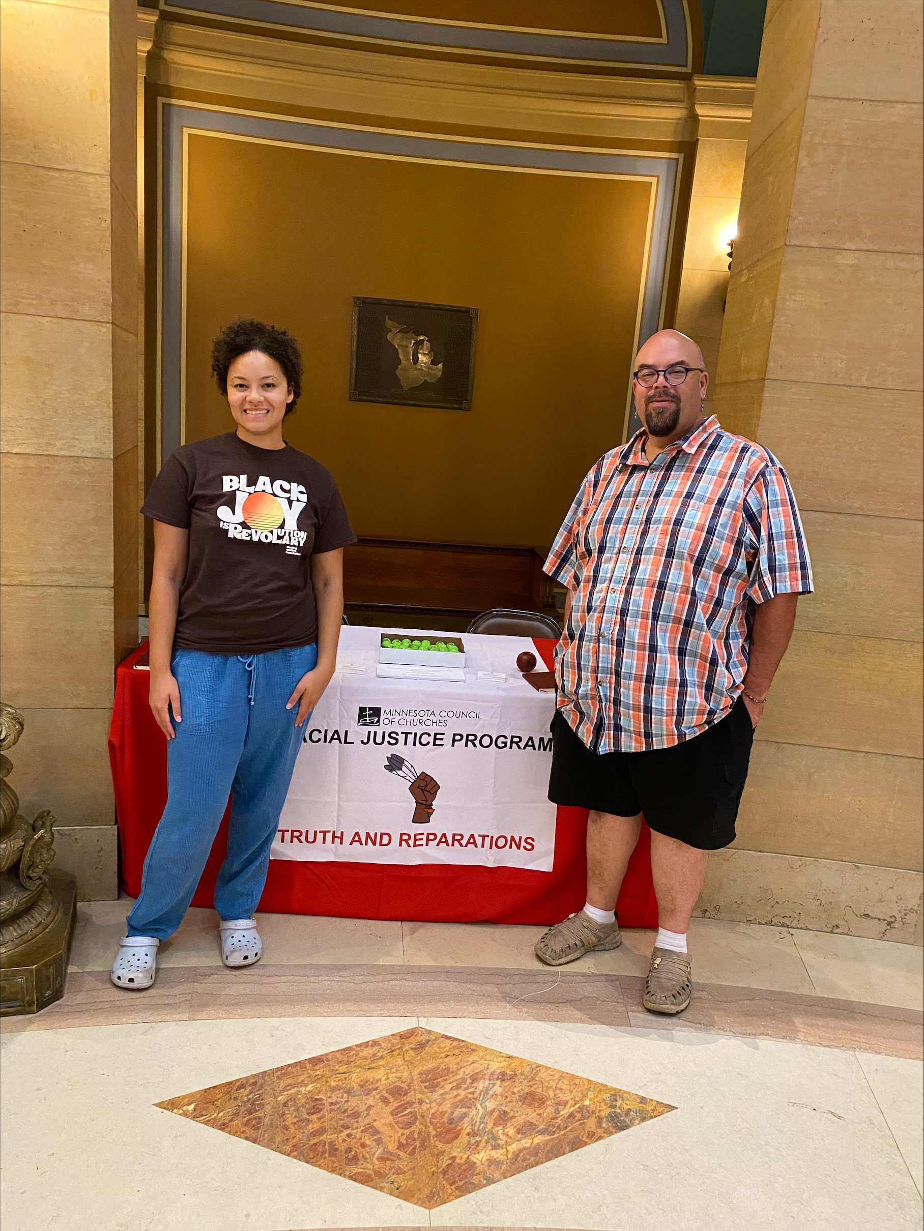 Rev. Jim Bear Jacobs, Co-Director of Racial Justice, and Racial Justice Administrative Assistant Phoebe McGowan in front of the MCC table in the Capitol Rotunda