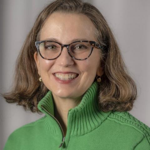A woman with brown hair and a green sweater smiles at the viewer.